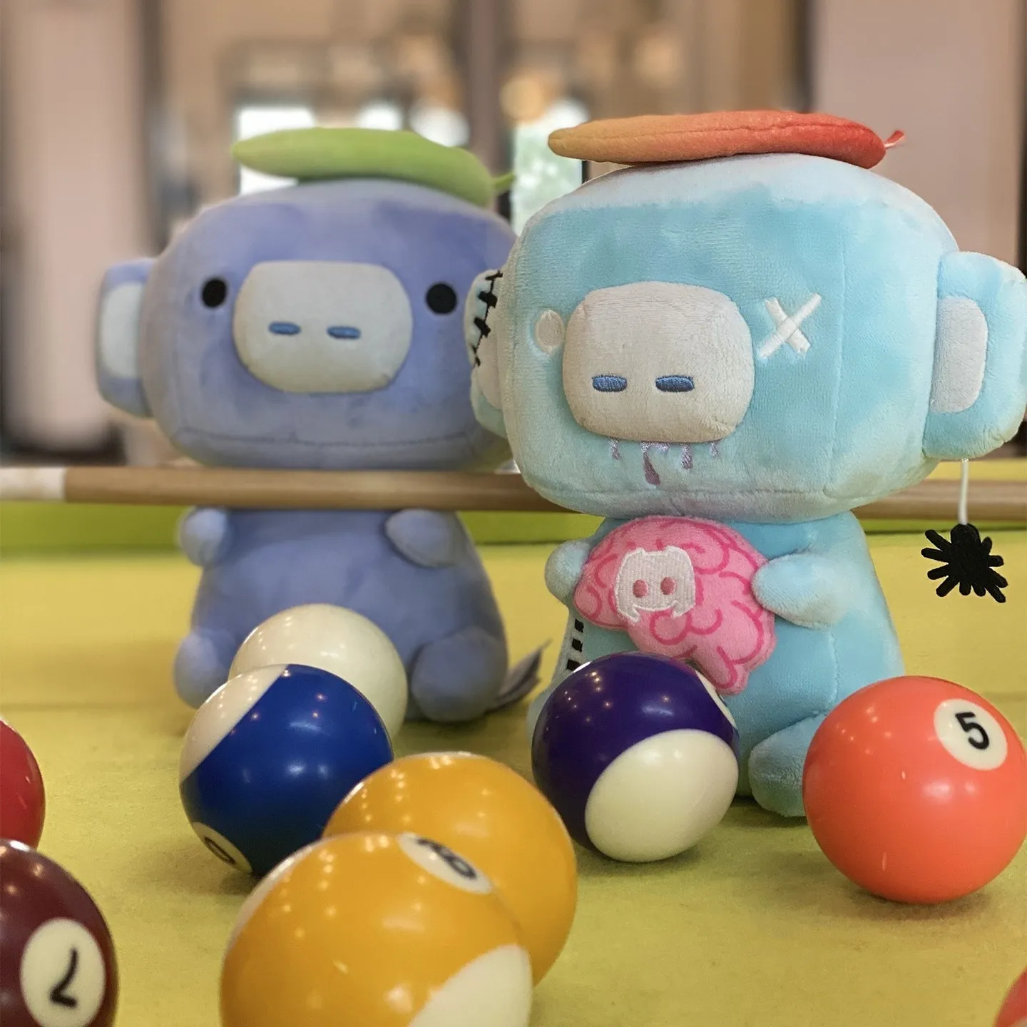 Zombie Wumpus and classic Wumpus plush toys on a pool table